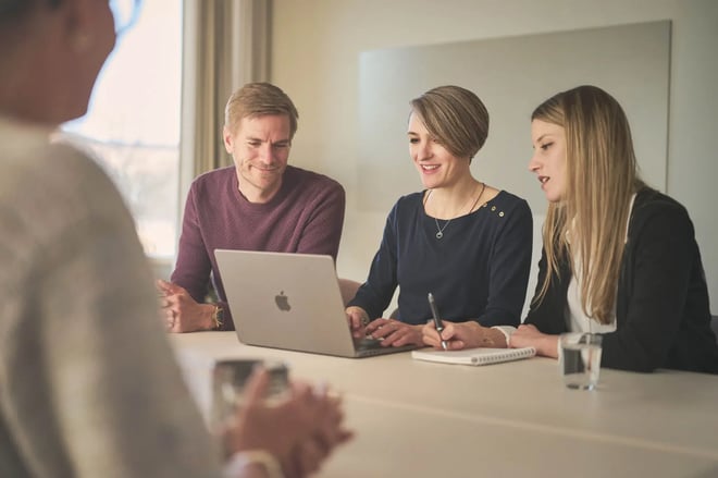 Members of the Pharmetheus Quality Control and Medical Writing team gathered around a laptop and notepad during a collaborative review meeting in a bright conference room.